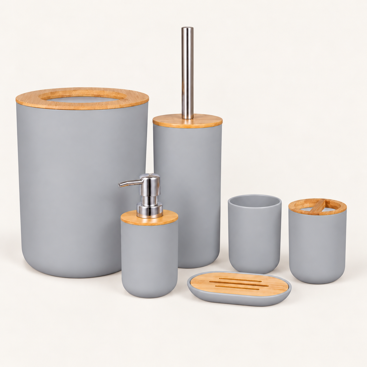 Grey six-piece bamboo bathroom accessories set with open-top waste bin, silver pump dispenser, toothbrush holder, tumbler, toilet brush and soap dish on warm cream background